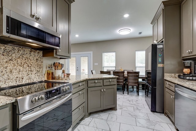 kitchen featuring gray cabinets, light stone countertops, appliances with stainless steel finishes, and tasteful backsplash