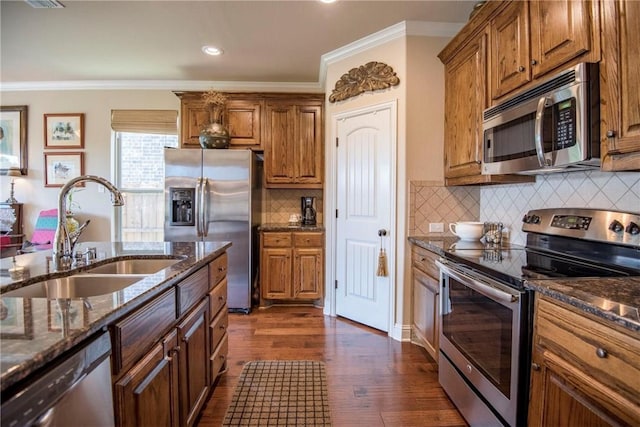 kitchen featuring appliances with stainless steel finishes, dark hardwood / wood-style flooring, ornamental molding, dark stone counters, and sink