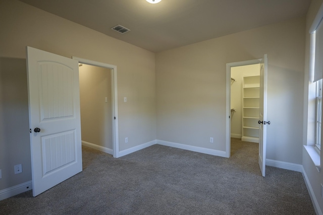 unfurnished bedroom with dark colored carpet, a walk in closet, and a closet