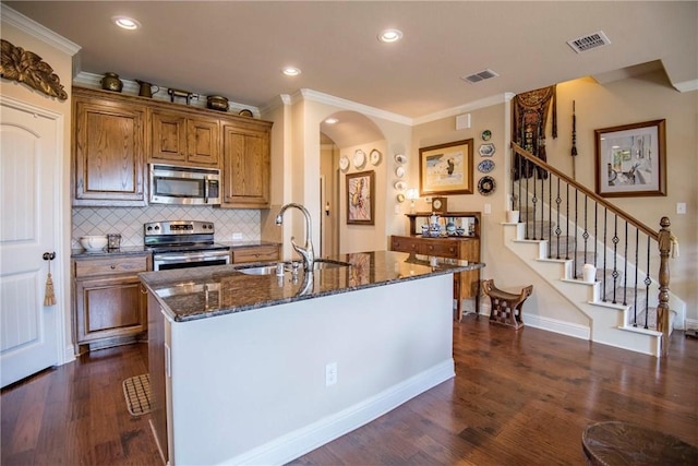 kitchen with appliances with stainless steel finishes, crown molding, sink, a center island with sink, and dark hardwood / wood-style floors