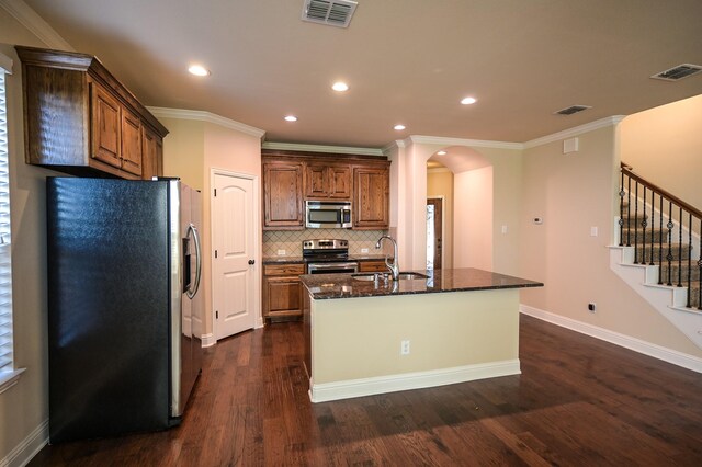 kitchen featuring dark stone counters, sink, dark hardwood / wood-style floors, an island with sink, and appliances with stainless steel finishes