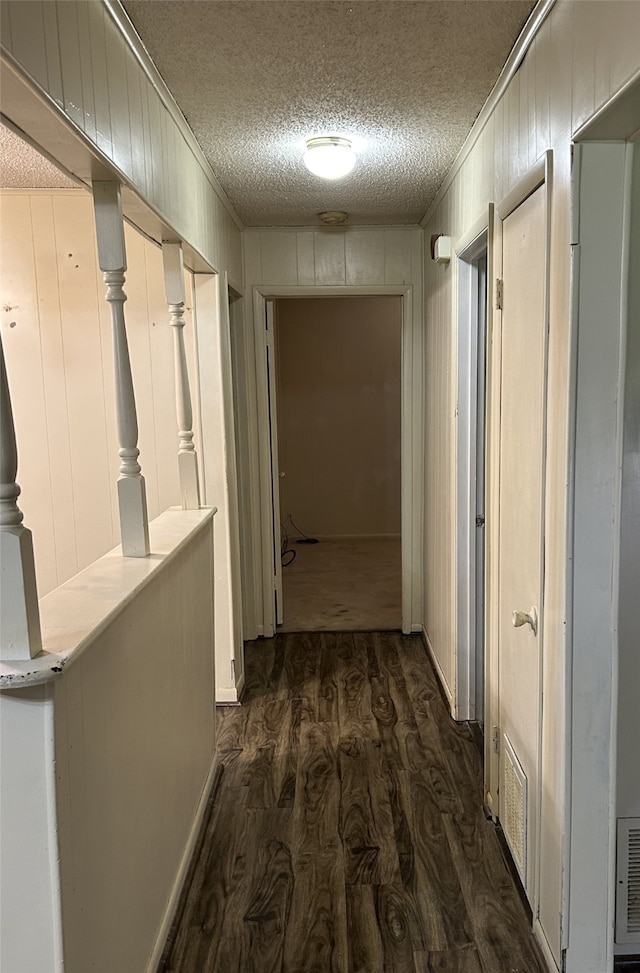 corridor with a textured ceiling, wood walls, and dark hardwood / wood-style floors