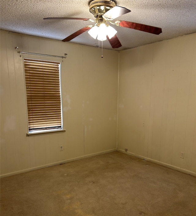 spare room with ceiling fan, wood walls, light colored carpet, and a textured ceiling