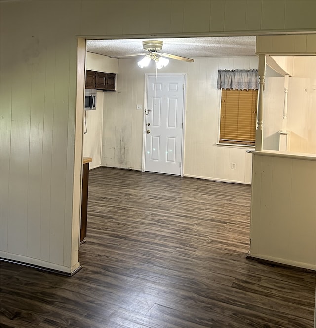 entryway with wood walls, dark hardwood / wood-style floors, ceiling fan, and a textured ceiling