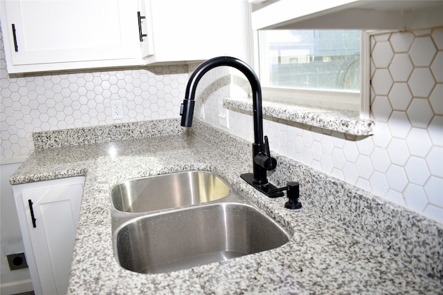 room details with backsplash, light stone counters, white cabinetry, and sink