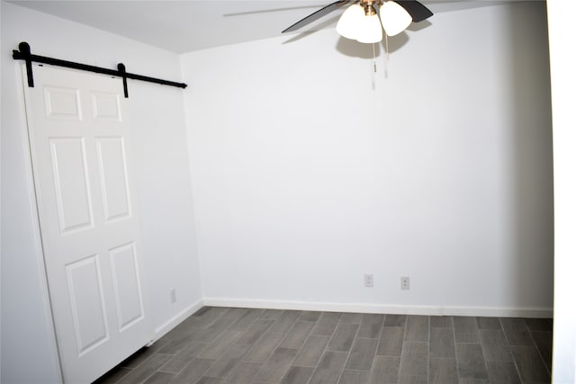 empty room featuring a barn door, dark hardwood / wood-style floors, and ceiling fan