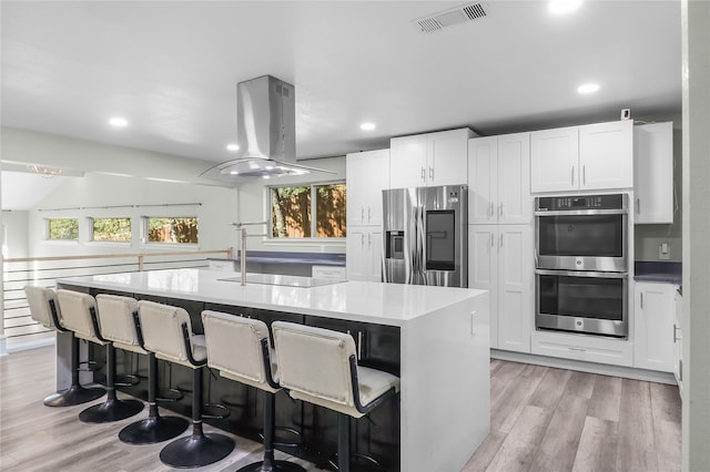 kitchen featuring white cabinetry, stainless steel appliances, island exhaust hood, a kitchen bar, and a center island with sink