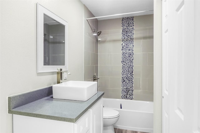 full bathroom with tiled shower / bath, vanity, wood-type flooring, and toilet