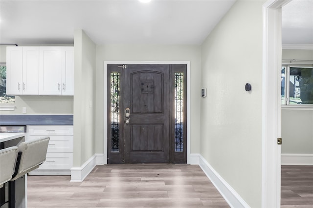 foyer with a healthy amount of sunlight, light wood-type flooring, and crown molding