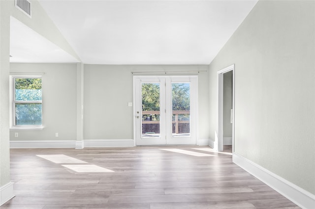 unfurnished room with light hardwood / wood-style floors, vaulted ceiling, and a healthy amount of sunlight