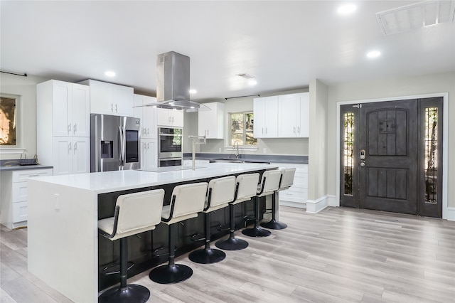 kitchen with island range hood, white cabinets, a kitchen breakfast bar, appliances with stainless steel finishes, and a kitchen island