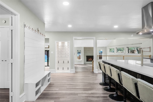 interior space with wood-type flooring, a tile fireplace, and wall chimney range hood