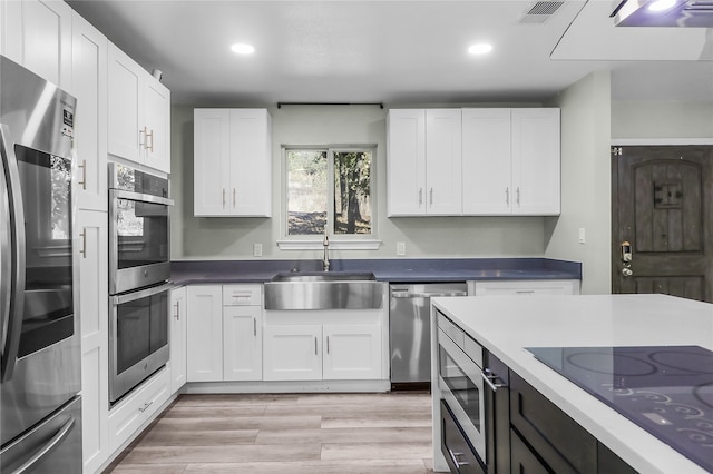 kitchen with white cabinets, appliances with stainless steel finishes, light hardwood / wood-style flooring, and sink