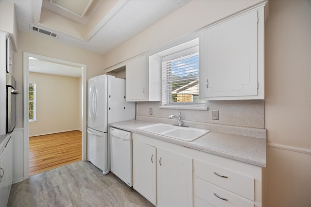 kitchen with white appliances, white cabinets, sink, light hardwood / wood-style flooring, and a textured ceiling