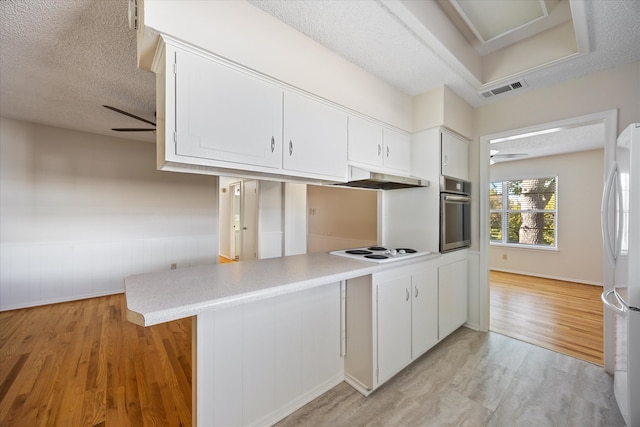 kitchen featuring a textured ceiling, kitchen peninsula, white cabinetry, and white appliances