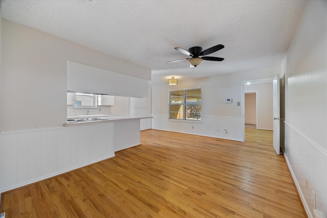 unfurnished living room with a textured ceiling, light hardwood / wood-style flooring, and ceiling fan