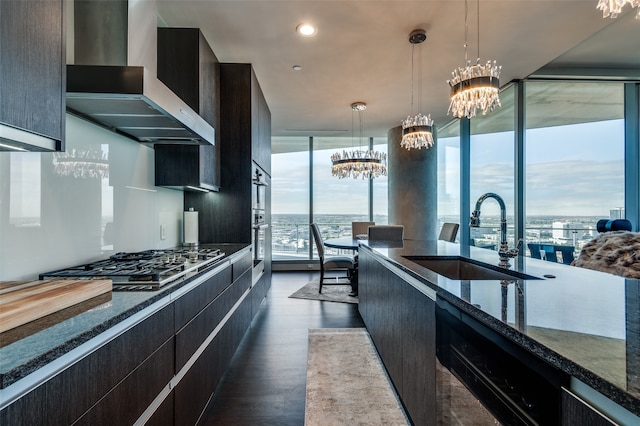 kitchen with sink, dark wood-type flooring, wall chimney range hood, an inviting chandelier, and decorative light fixtures