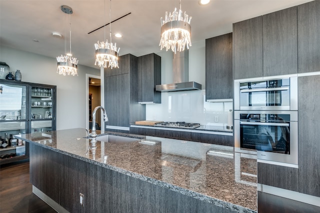 kitchen with sink, wall chimney range hood, dark hardwood / wood-style floors, dark stone counters, and decorative light fixtures