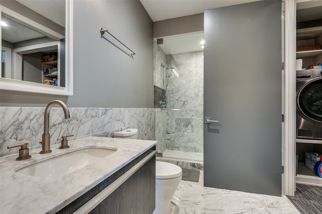 bathroom featuring toilet, washer / dryer, tiled shower, and vanity