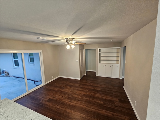 empty room featuring a textured ceiling, ceiling fan, built in features, and dark wood-type flooring