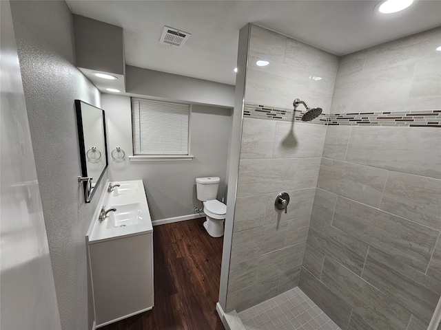 bathroom with hardwood / wood-style flooring, vanity, toilet, and tiled shower