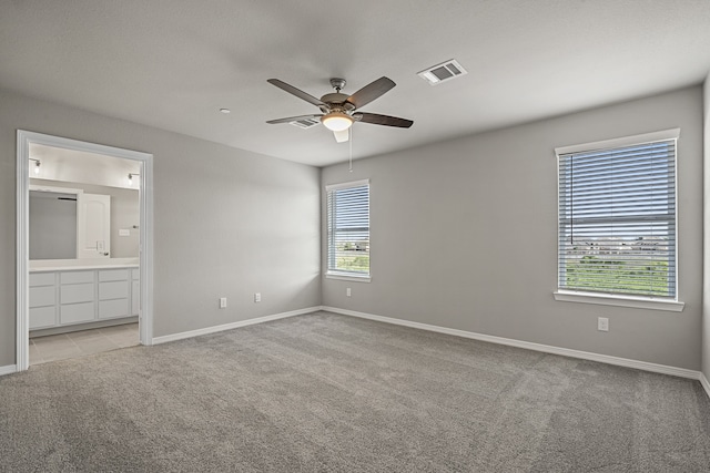 unfurnished bedroom with ensuite bath, ceiling fan, light carpet, and multiple windows