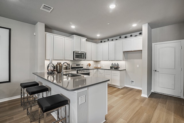 kitchen with stainless steel appliances, kitchen peninsula, light hardwood / wood-style floors, a breakfast bar, and white cabinets