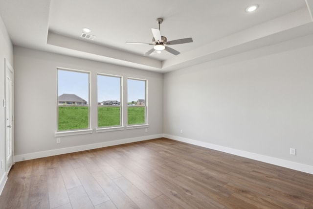 empty room with hardwood / wood-style flooring, ceiling fan, and a raised ceiling