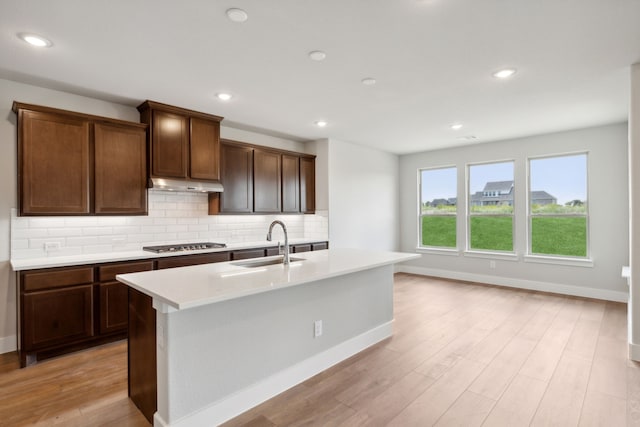 kitchen featuring a kitchen island with sink, sink, tasteful backsplash, light hardwood / wood-style floors, and stainless steel gas cooktop