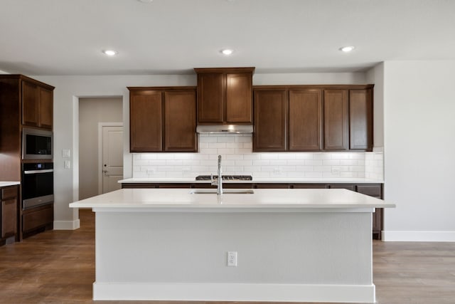 kitchen featuring backsplash, a kitchen island with sink, wood-type flooring, and appliances with stainless steel finishes