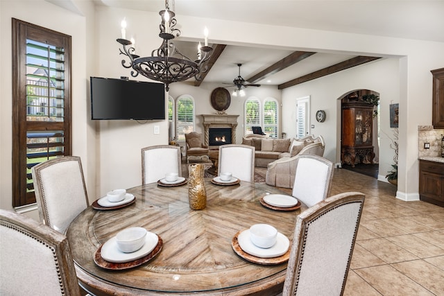 tiled dining room with beam ceiling and ceiling fan with notable chandelier