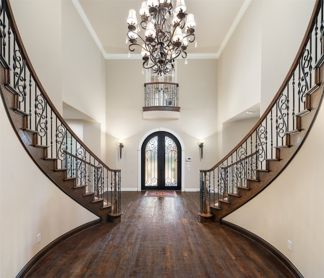 entryway featuring french doors, a towering ceiling, ornamental molding, a chandelier, and hardwood / wood-style floors