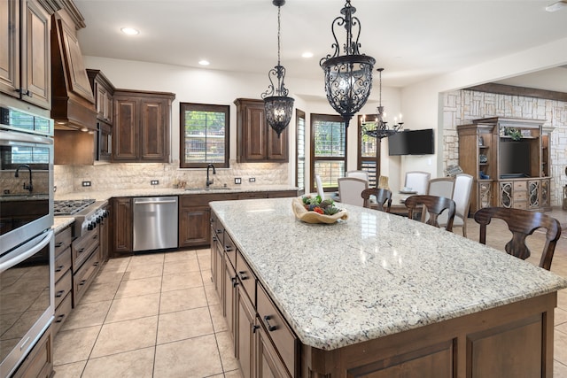 kitchen featuring decorative backsplash, hanging light fixtures, a center island, light stone counters, and stainless steel appliances