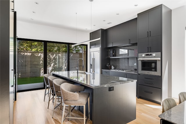 kitchen featuring sink, pendant lighting, a kitchen island with sink, a breakfast bar, and appliances with stainless steel finishes