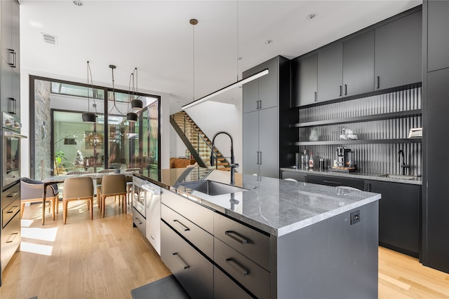 kitchen with sink, stainless steel oven, light hardwood / wood-style flooring, decorative light fixtures, and a center island with sink