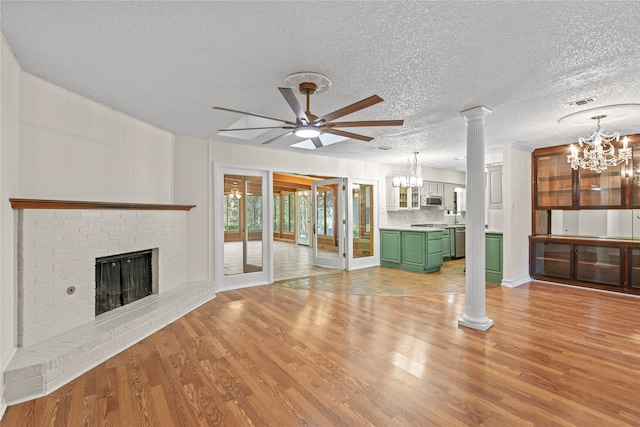 unfurnished living room with ornate columns, a textured ceiling, light hardwood / wood-style flooring, a fireplace, and ceiling fan with notable chandelier