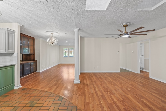 unfurnished living room with ornate columns, hardwood / wood-style flooring, and ceiling fan with notable chandelier