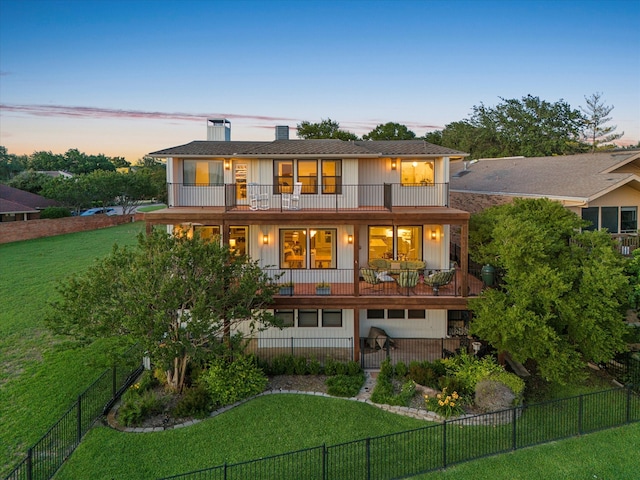 back house at dusk with a lawn and a balcony