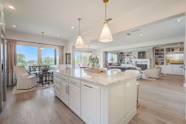 kitchen with a center island, hanging light fixtures, light wood-type flooring, light stone counters, and white cabinetry