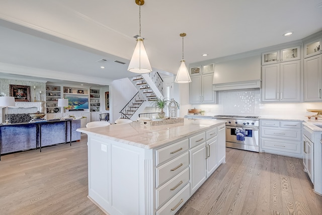 kitchen featuring high end range, pendant lighting, white cabinets, light hardwood / wood-style floors, and a kitchen island