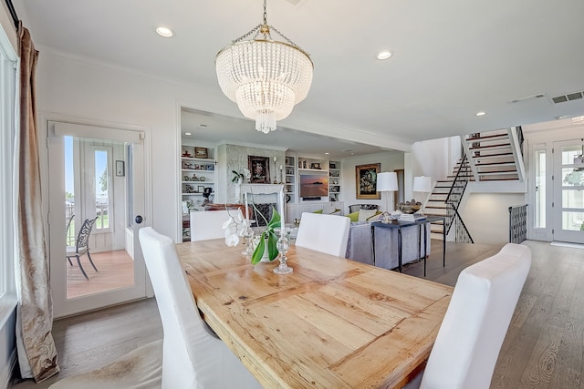 dining room featuring built in shelves, a large fireplace, a notable chandelier, and light wood-type flooring