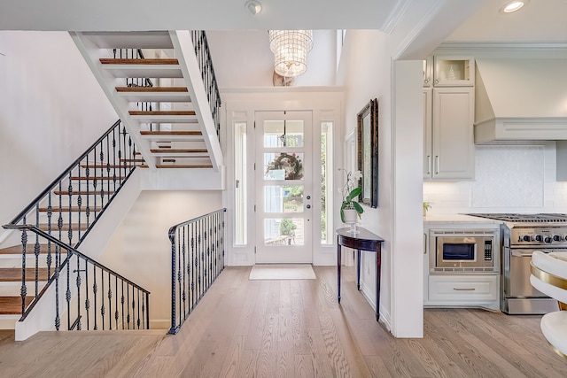 entrance foyer featuring light wood-type flooring, crown molding, and an inviting chandelier