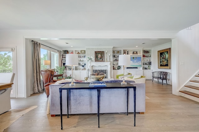 living room with built in shelves, light wood-type flooring, a large fireplace, and crown molding