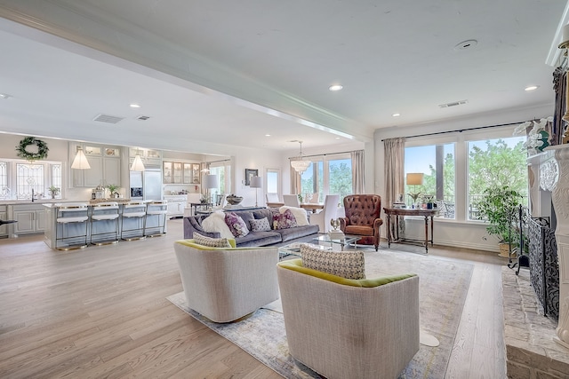 living room with sink, light wood-type flooring, crown molding, and an inviting chandelier