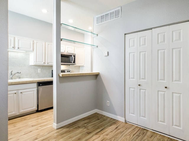 kitchen with appliances with stainless steel finishes, light wood-type flooring, and white cabinetry