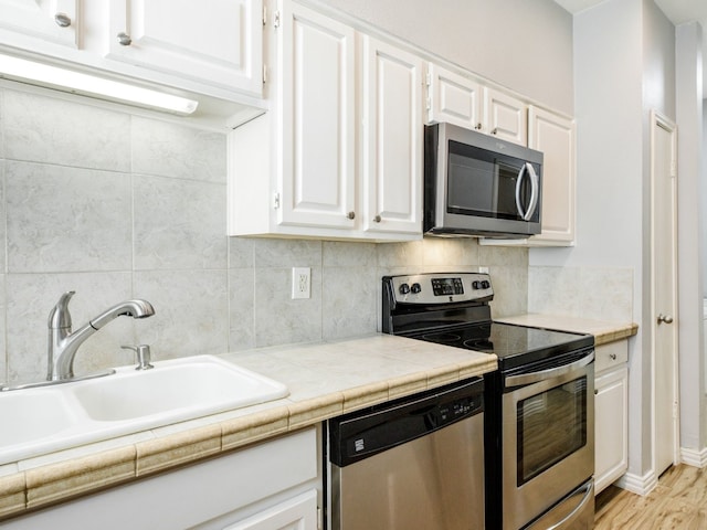 kitchen featuring tile countertops, sink, appliances with stainless steel finishes, light hardwood / wood-style floors, and white cabinetry