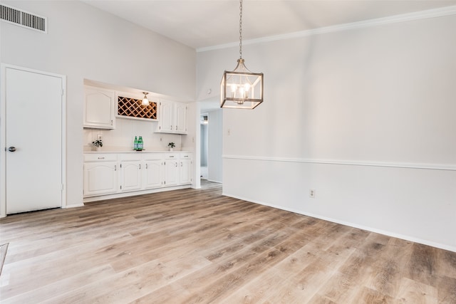 unfurnished dining area featuring crown molding, light hardwood / wood-style flooring, and a towering ceiling