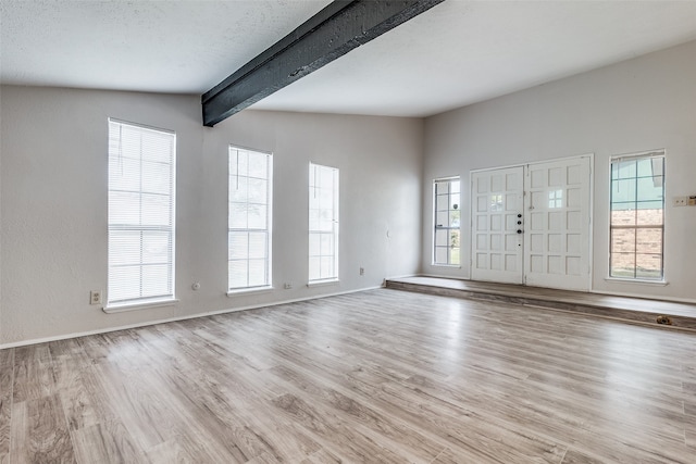 entrance foyer featuring light wood-type flooring, a textured ceiling, vaulted ceiling with beams, and a wealth of natural light