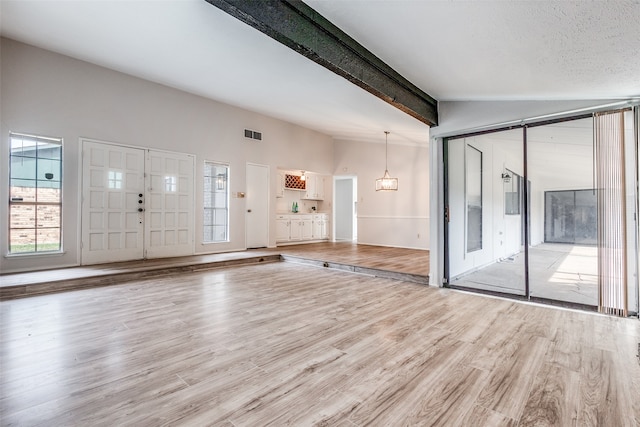 foyer entrance with vaulted ceiling with beams, a wealth of natural light, light hardwood / wood-style floors, and a textured ceiling