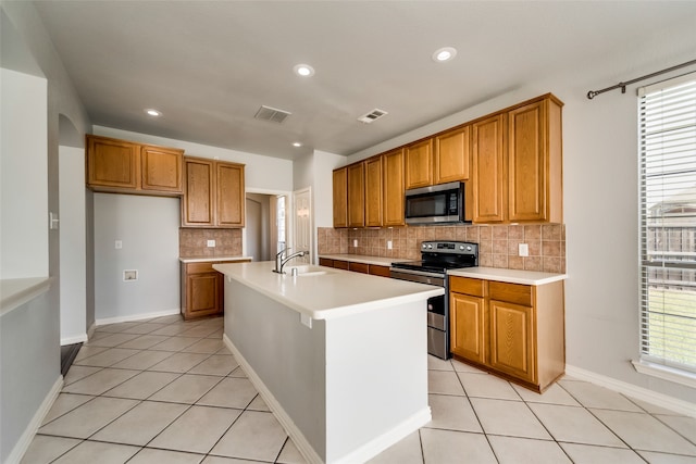 kitchen with sink, decorative backsplash, an island with sink, light tile patterned flooring, and stainless steel appliances